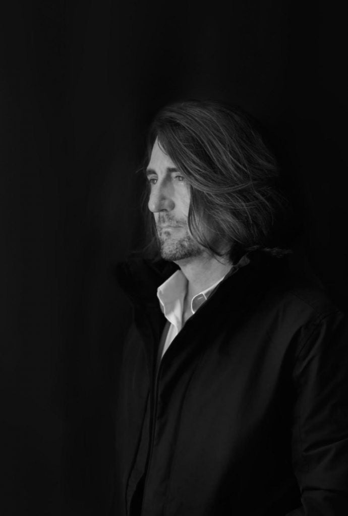 Black and white portrait of Jörg Bräuer with long hair against a dark background