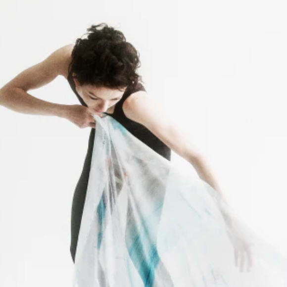 A dancer in a black leotard draping a silk scarf across a white floor