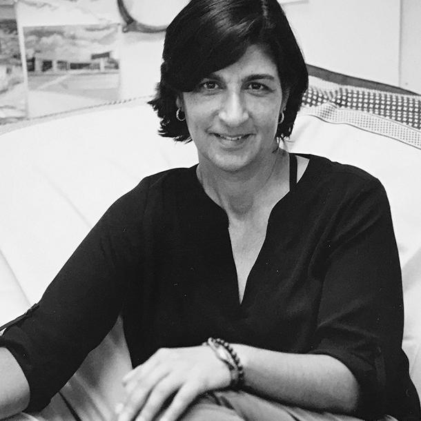 black and white photo of Deni Javas smiling with her legs up on a couch