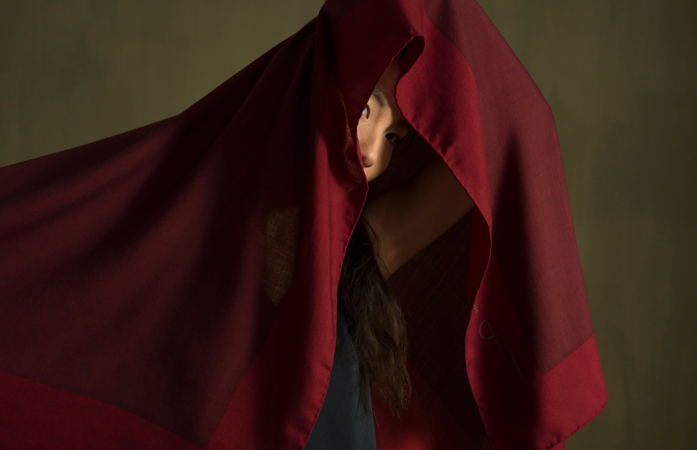 a woman mostly covered by Darshana Shilpi's Intonation 1 scarf, in reds. Intense colour blocks are printed using the silk-screen method onto soft, rich wool fabric