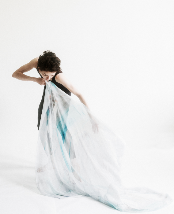 A dancer in a black leotard draping a silk scarf across a white floor