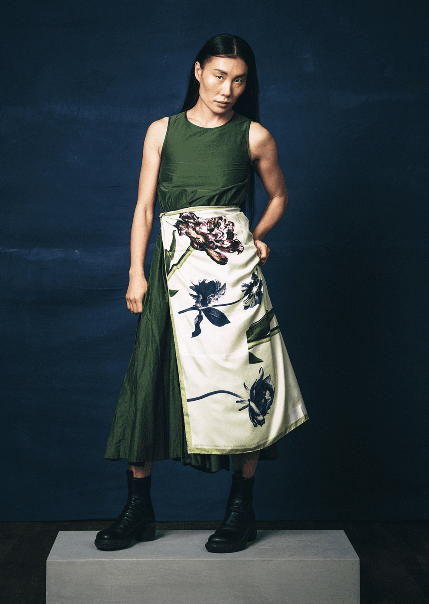 Person wearing a green top and floral scarf by James T Murray as a skirt against a dark background