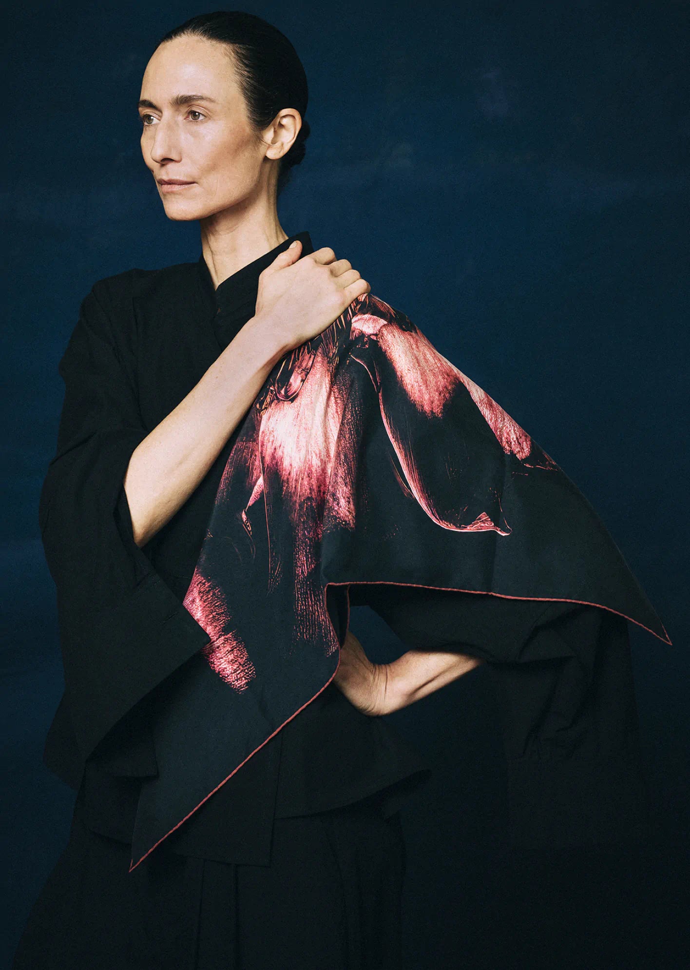 Woman wearing a black outfit with a red and pink patterned shawl by James T Murray against a dark background