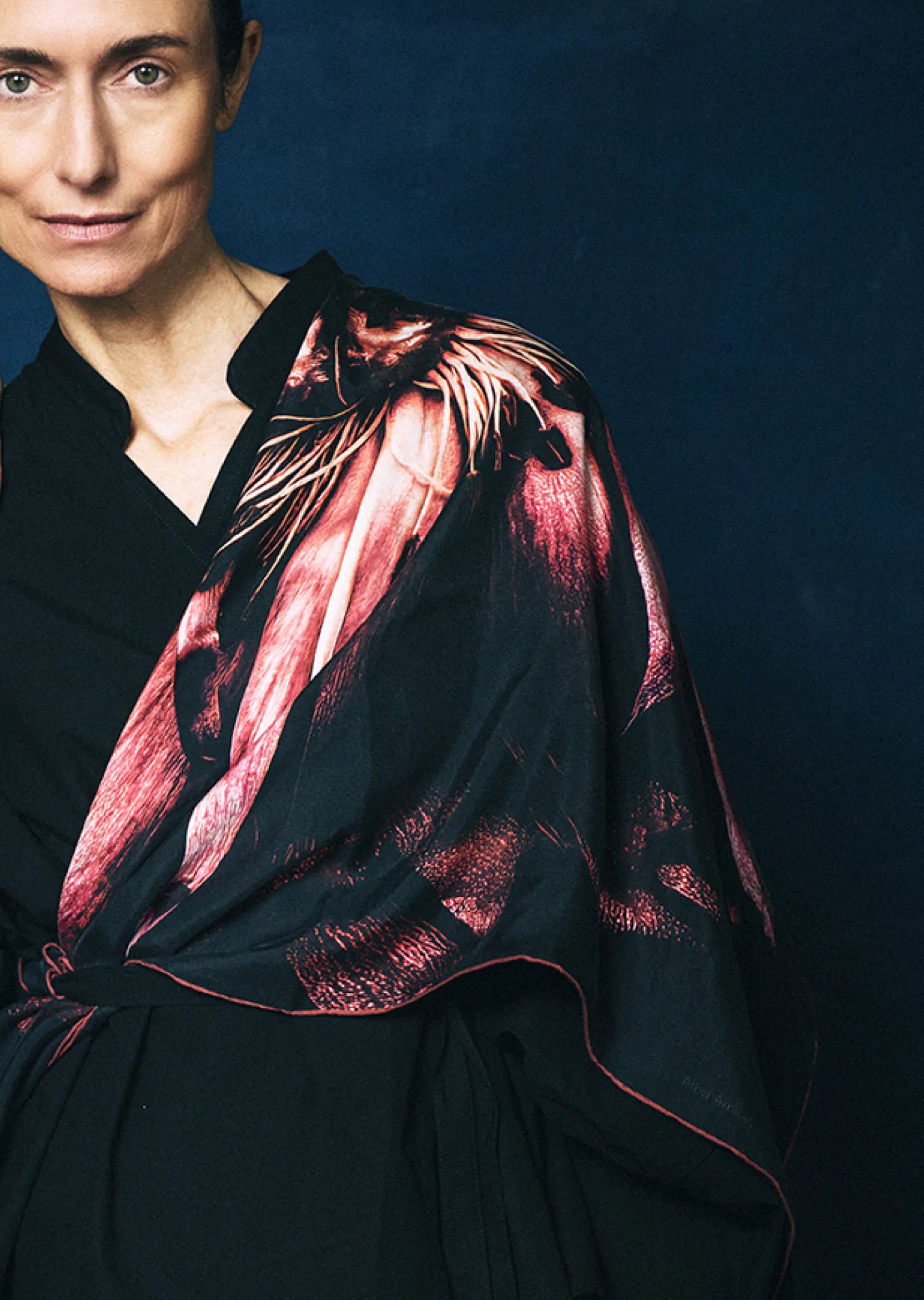 Woman wearing a black garment with a red patterned by James T Murray shawl against a dark background