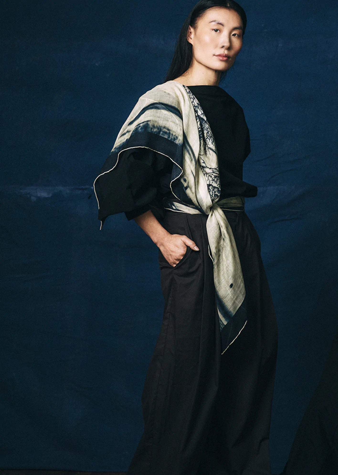 Person wearing a black outfit with a James T Murray patterned scarf against a dark blue background