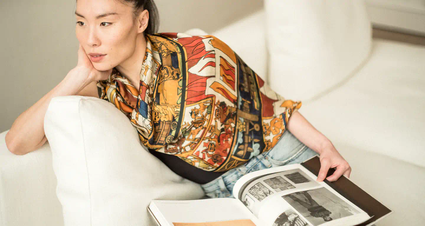 Woman sitting on a couch wearing a patterned scarf, Indian Carousel, holding a magazine.
