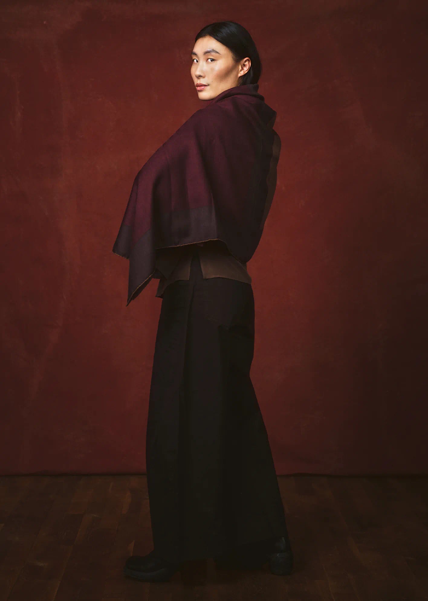 Person wearing a dark outfit with a draped scarf by Darshana Shilpi Rouget against a red background