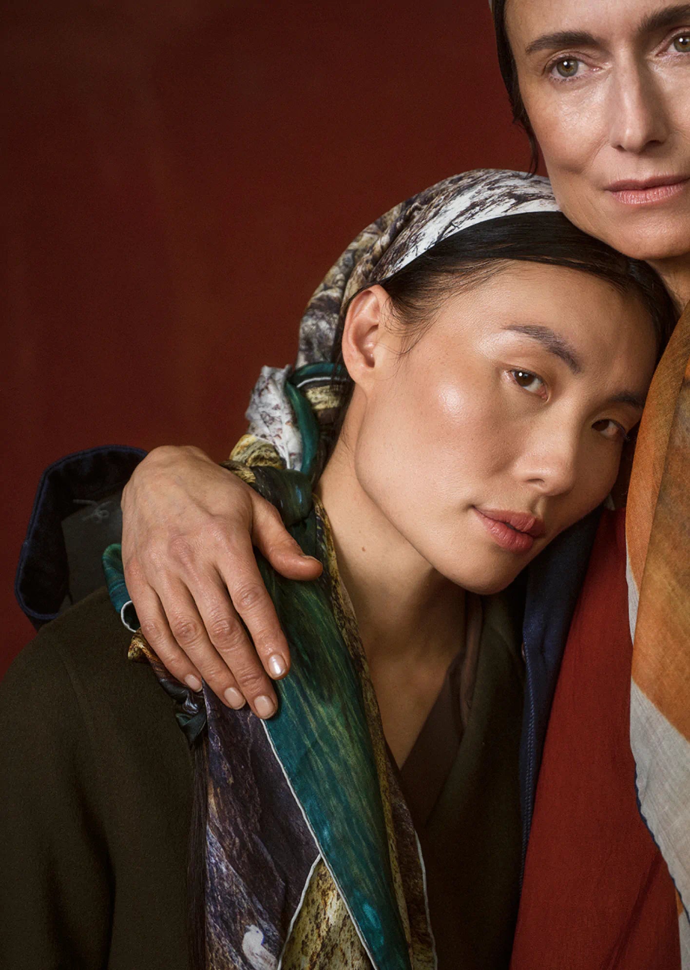 Two women wearing colorful scarves against a red background