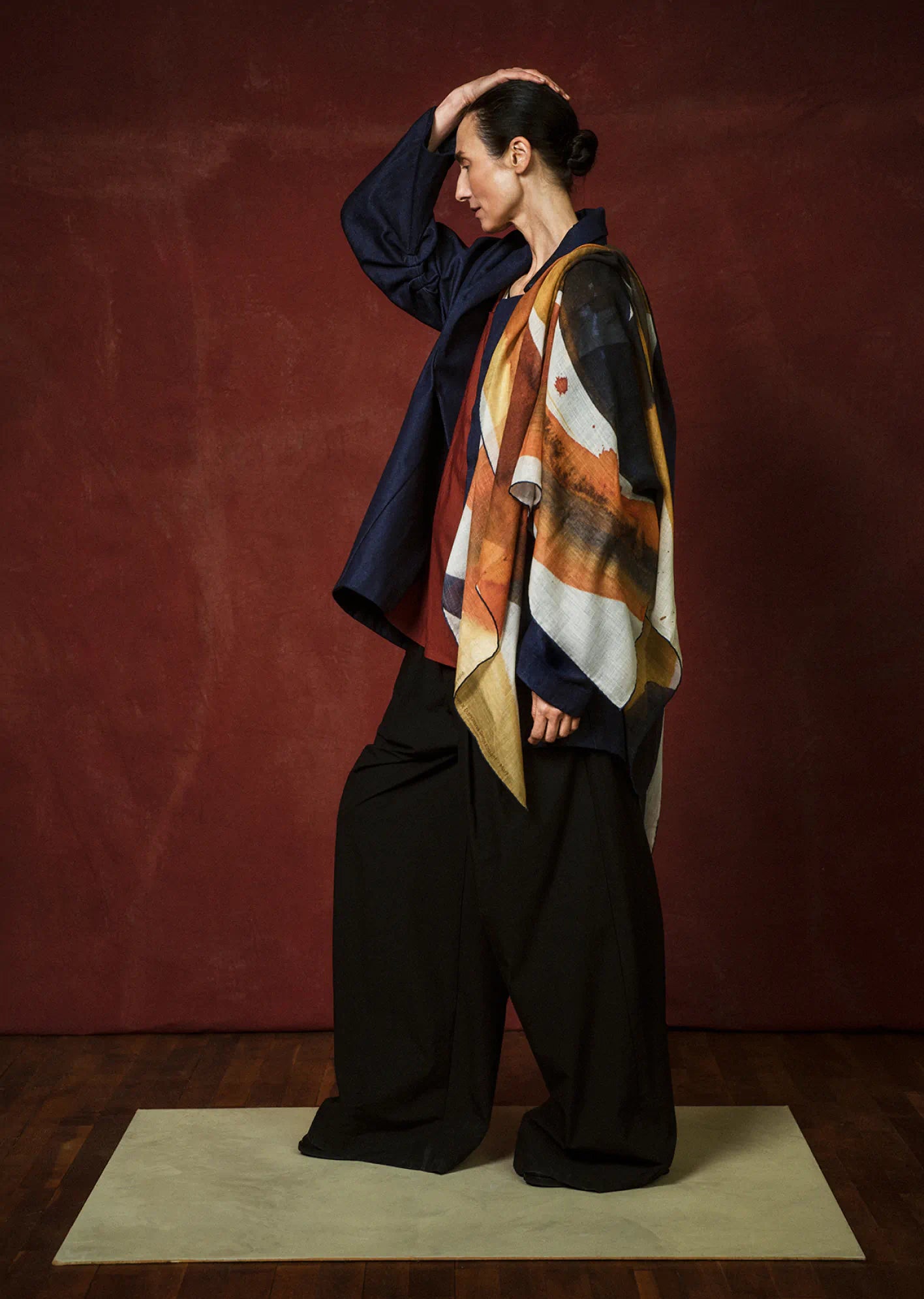 Person wearing a colorful scarf and dark outfit against a red background