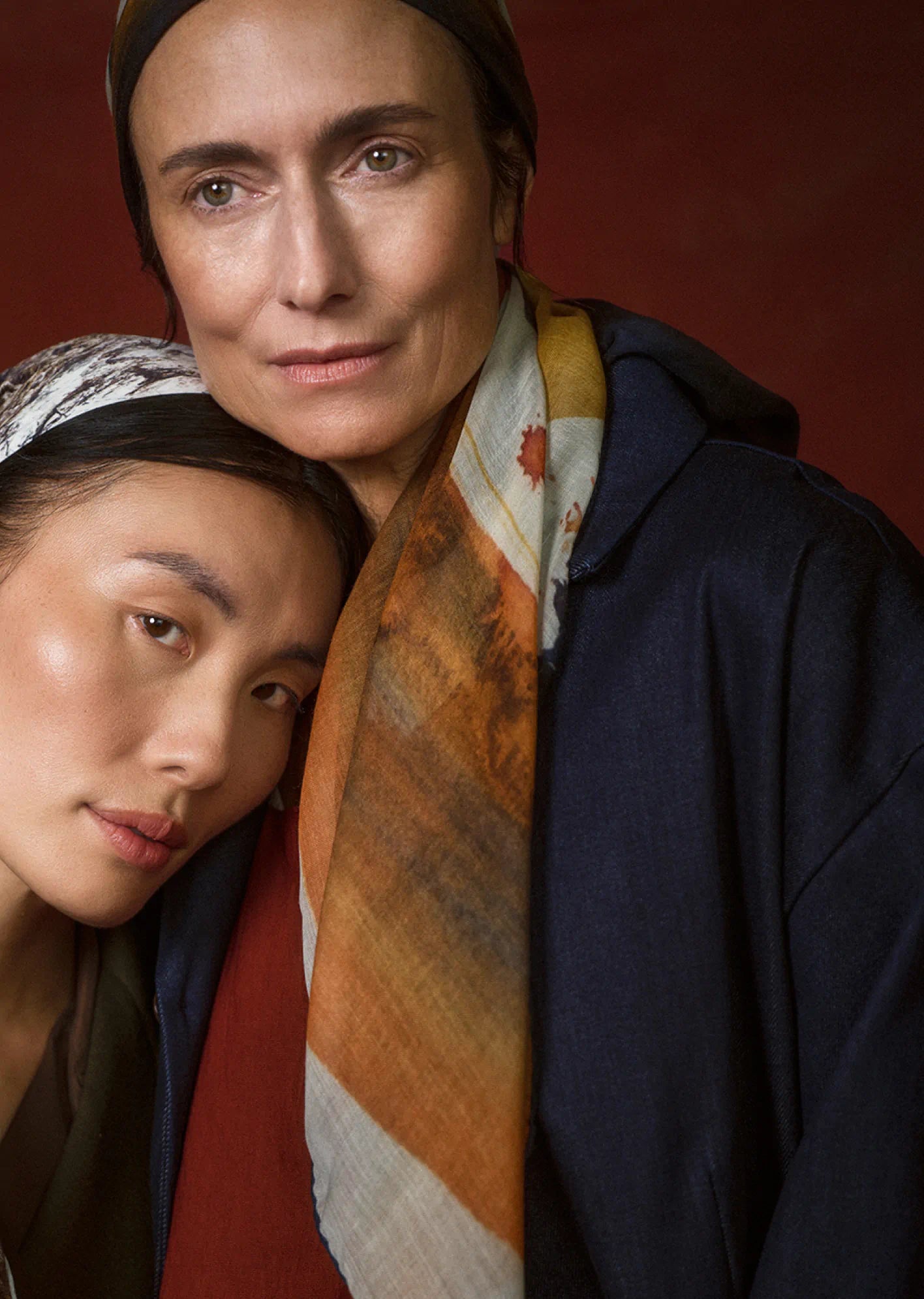 Two women wearing scarves against a red background
