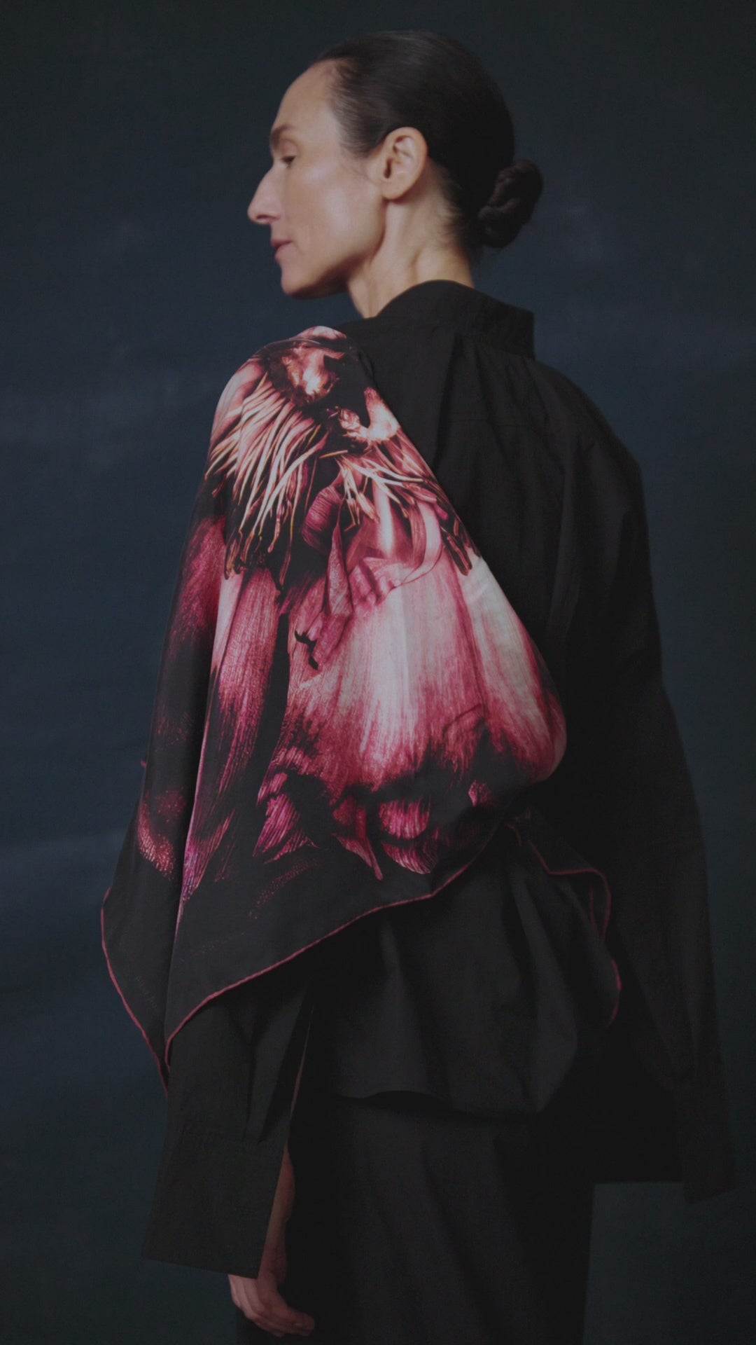 video of Woman wearing a black outfit with a red and pink patterned shawl by James T Murrayagainst a dark background