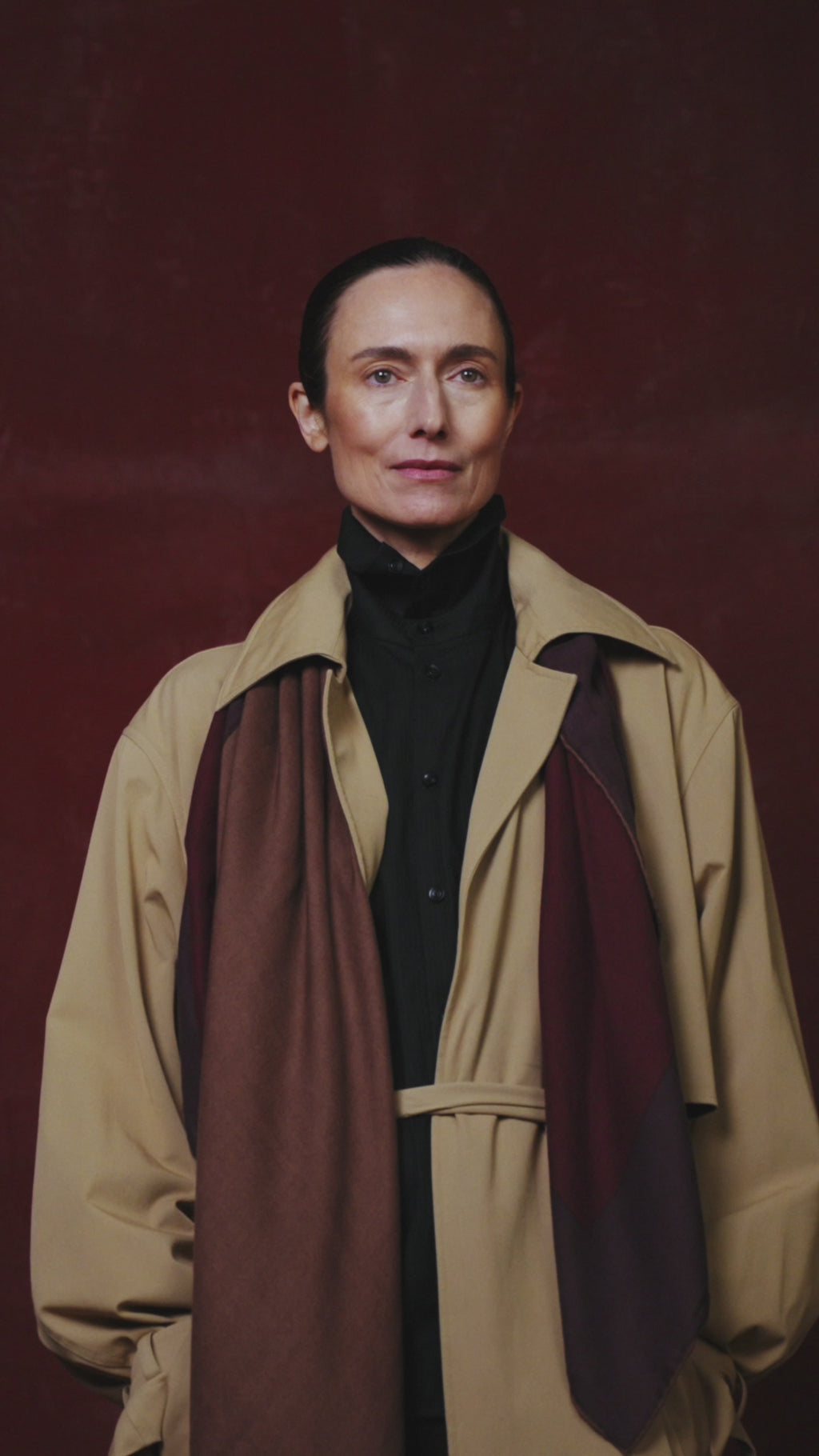 video of Woman wearing a beige trench coat with a dark scarf against a red background