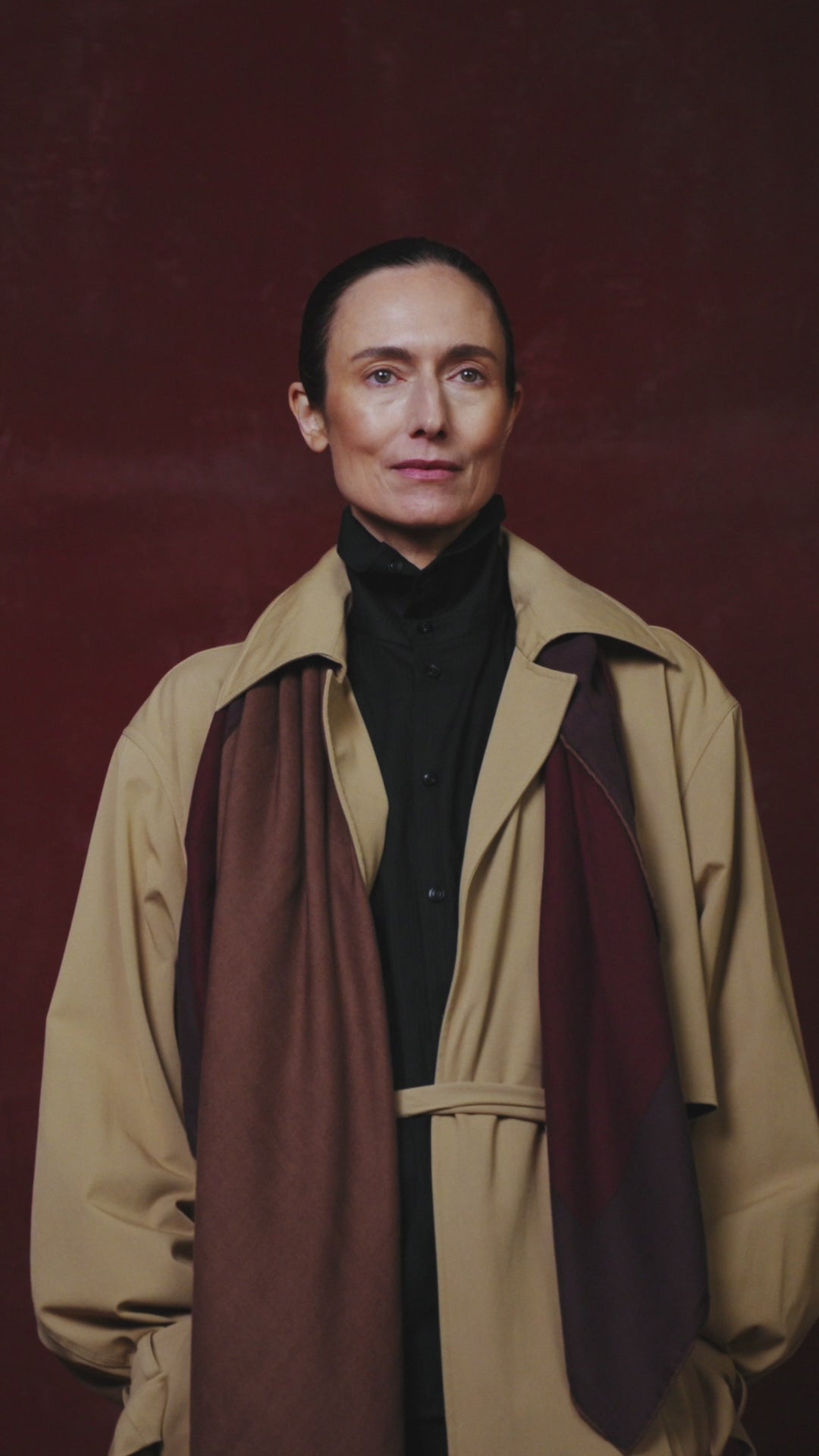 video of Woman wearing a beige trench coat with a dark scarf against a red background