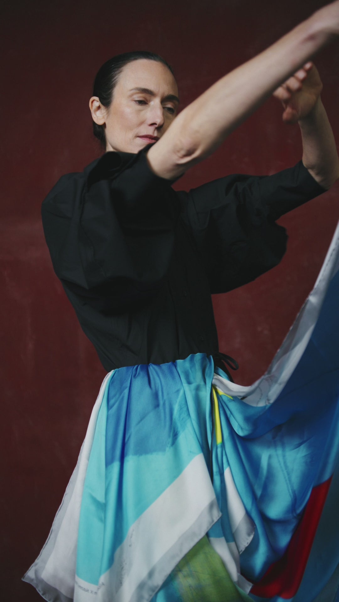 video of a Woman in a black top and colorful scarf by Naomi Frears against a dark red background