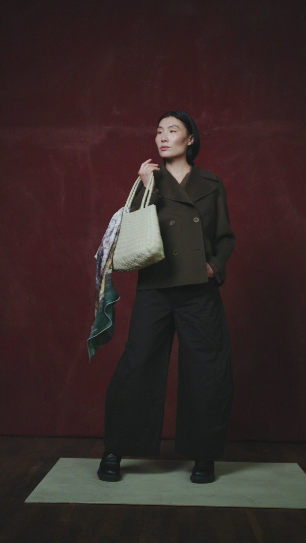 video of a person holding a large textured bag draped with an art scarf by Jorg Brauer with a scenic design against a dark red wall