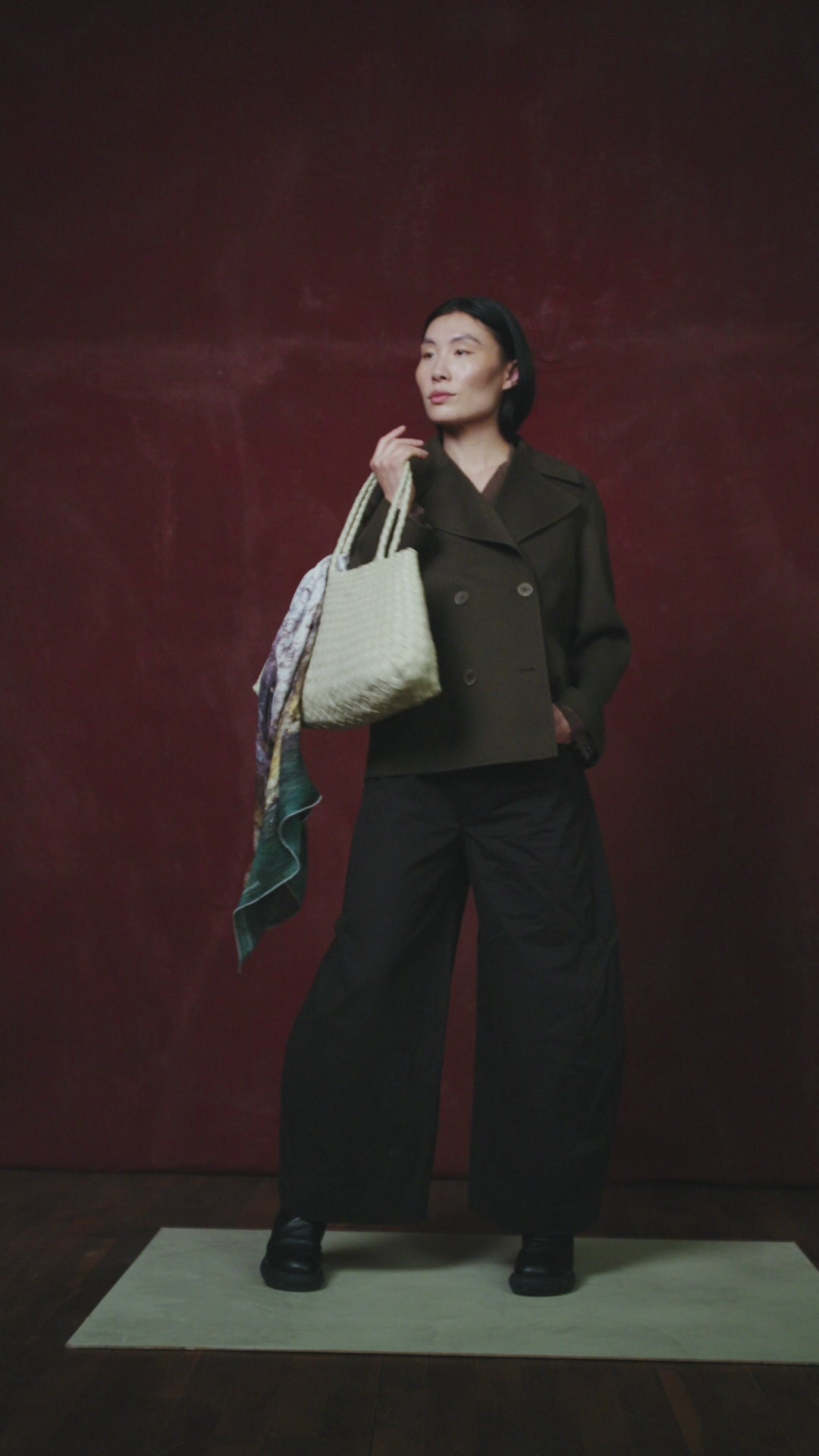 video of a person holding a large textured bag draped with an art scarf by Jorg Brauer with a scenic design against a dark red wall