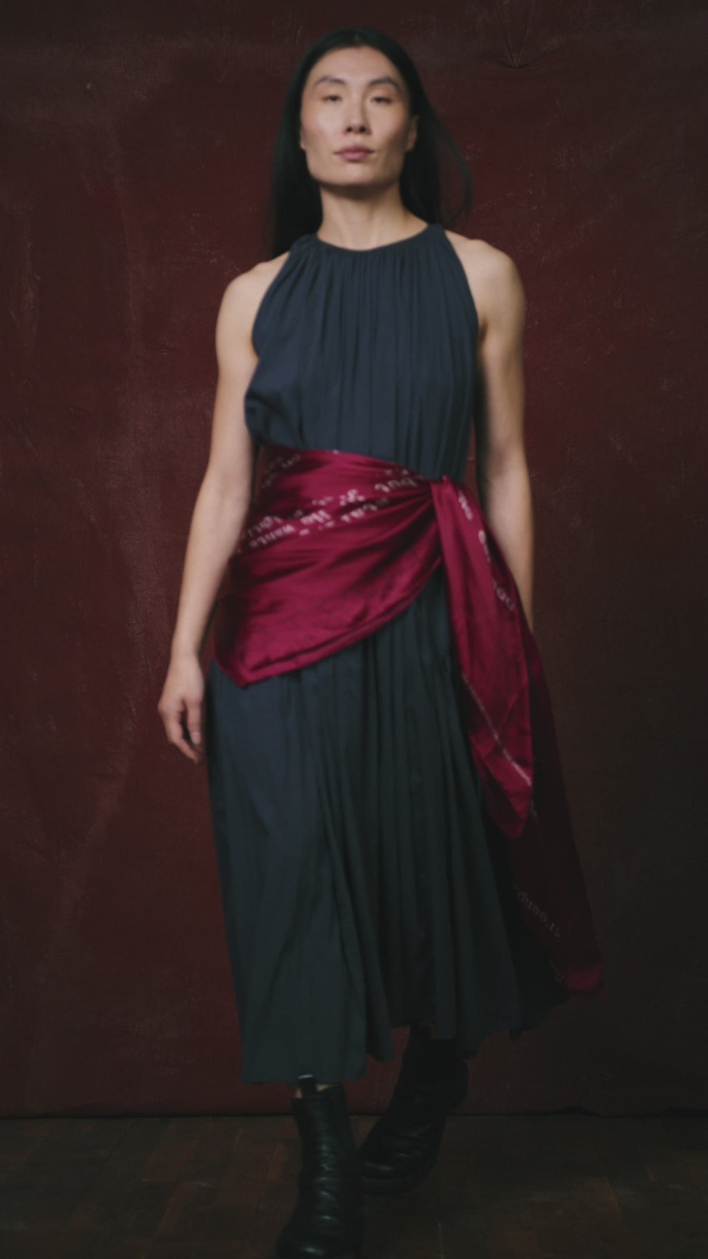 video of a Woman in a dark dress on a red background wearing a Ross Klavan text-based scarf in burgundy wrapped around her waist