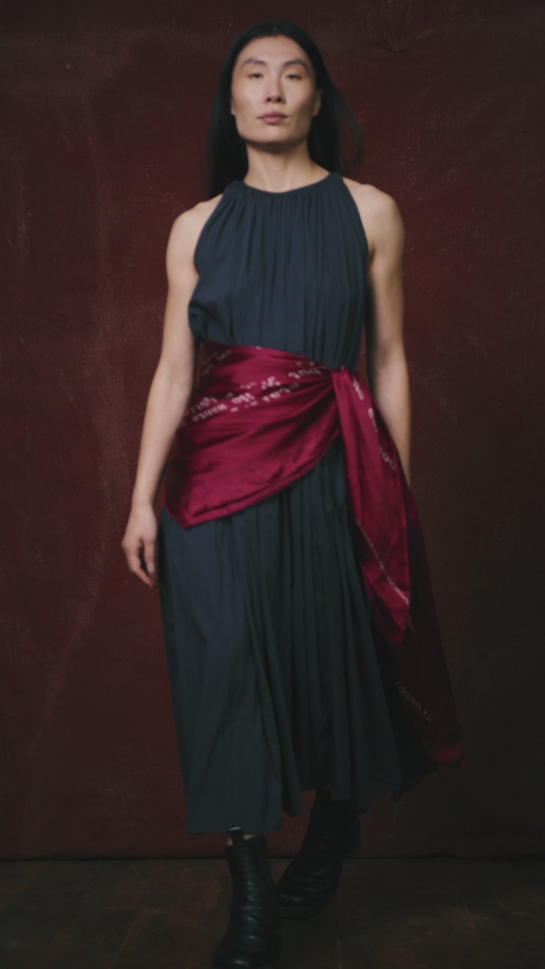 video of a Woman in a dark dress on a red background wearing a Ross Klavan text-based scarf in burgundy wrapped around her waist