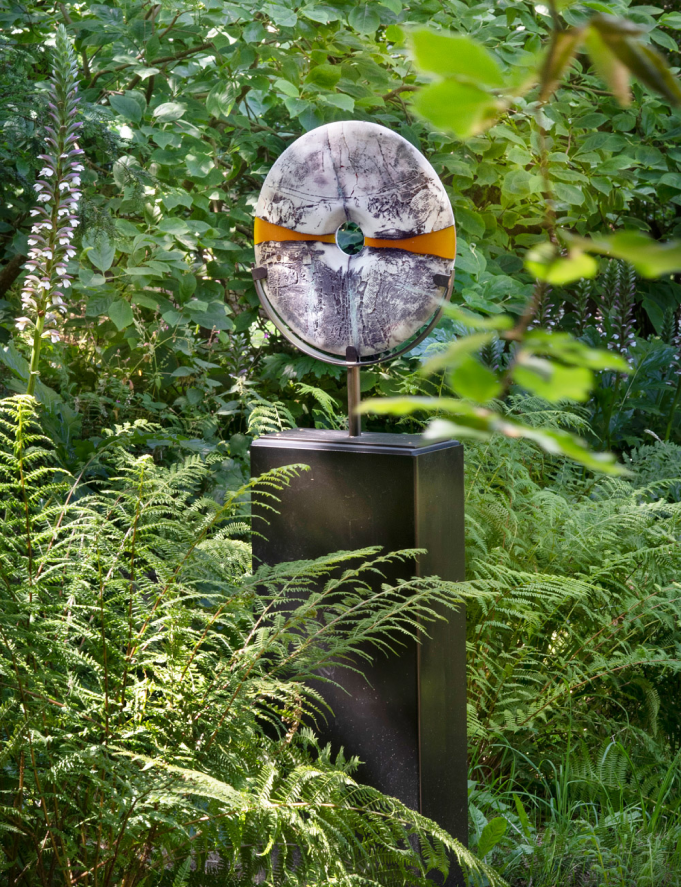 A doughnut shaped stone sculpture atom a large plinth nestled in the garden of Withiel