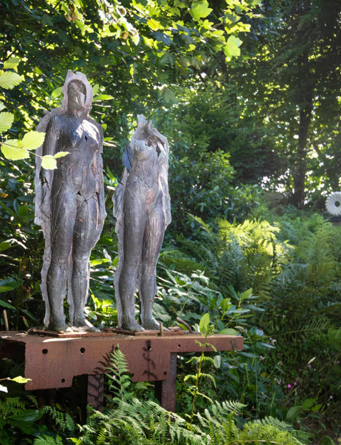 Two metal statues on a wooden platform in a garden setting with greenery.
